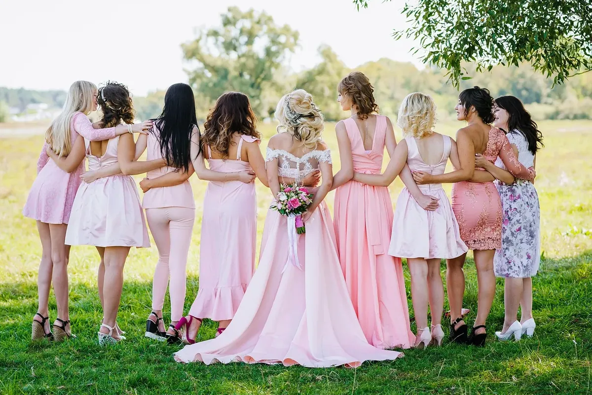 Bride and bridesmaids in pink dresses standing arm in arm in a meadow