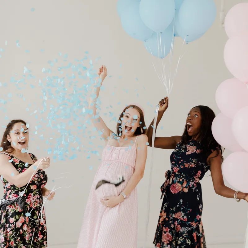 Friends celebrating a gender reveal with balloons and blue confetti, the kind of guest photos JollyPics collects