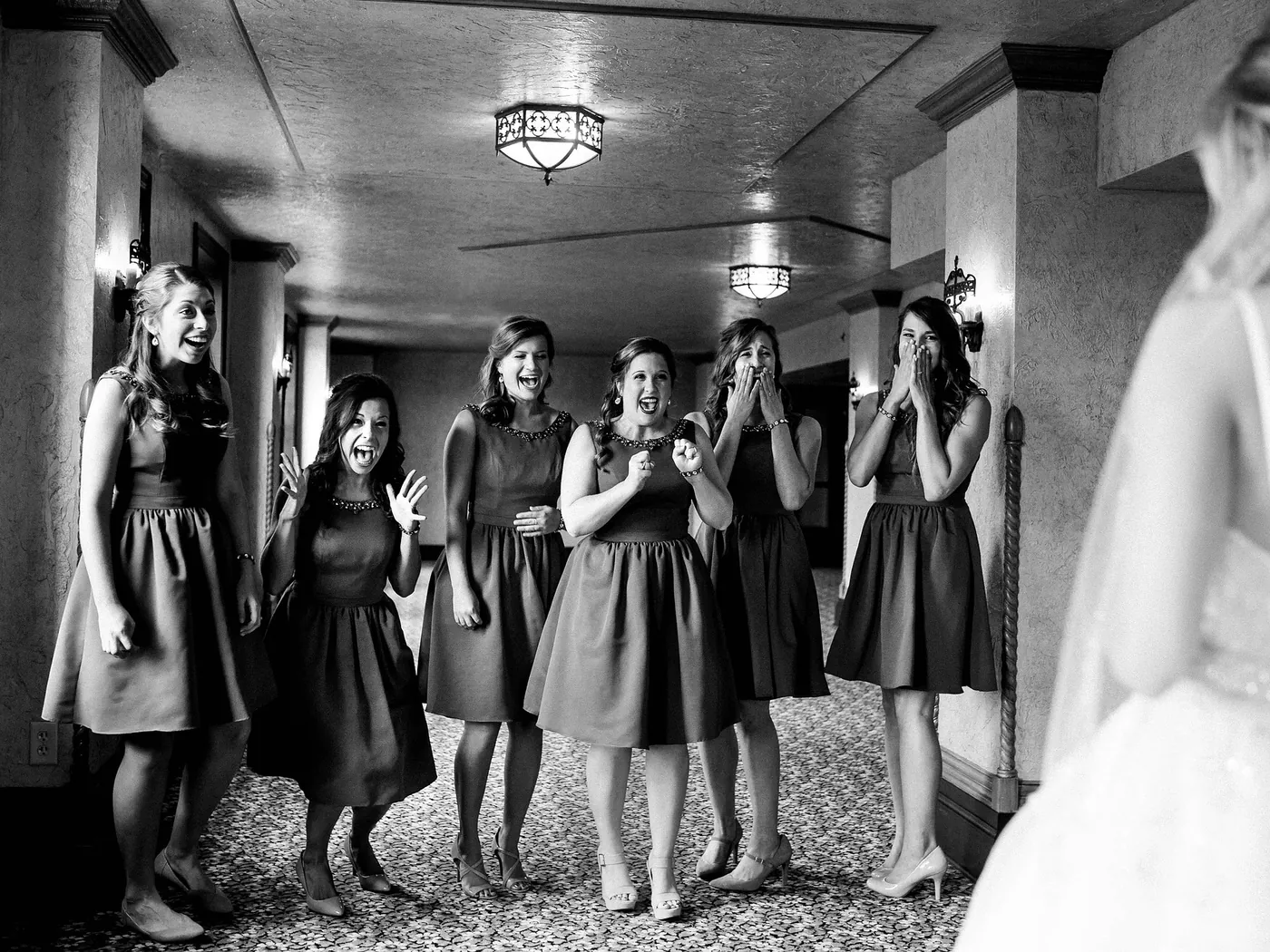 Bridesmaids reacting with joy as they see the bride in her dress